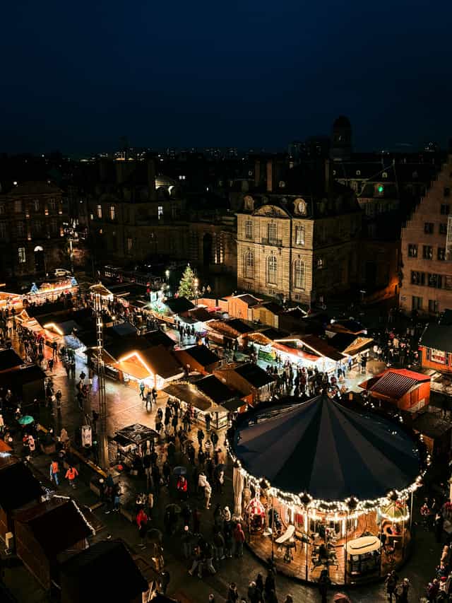Der Straßburger Weihnachtsmarkt von oben: erleuchtete Stände und das Karussell bei Nacht.