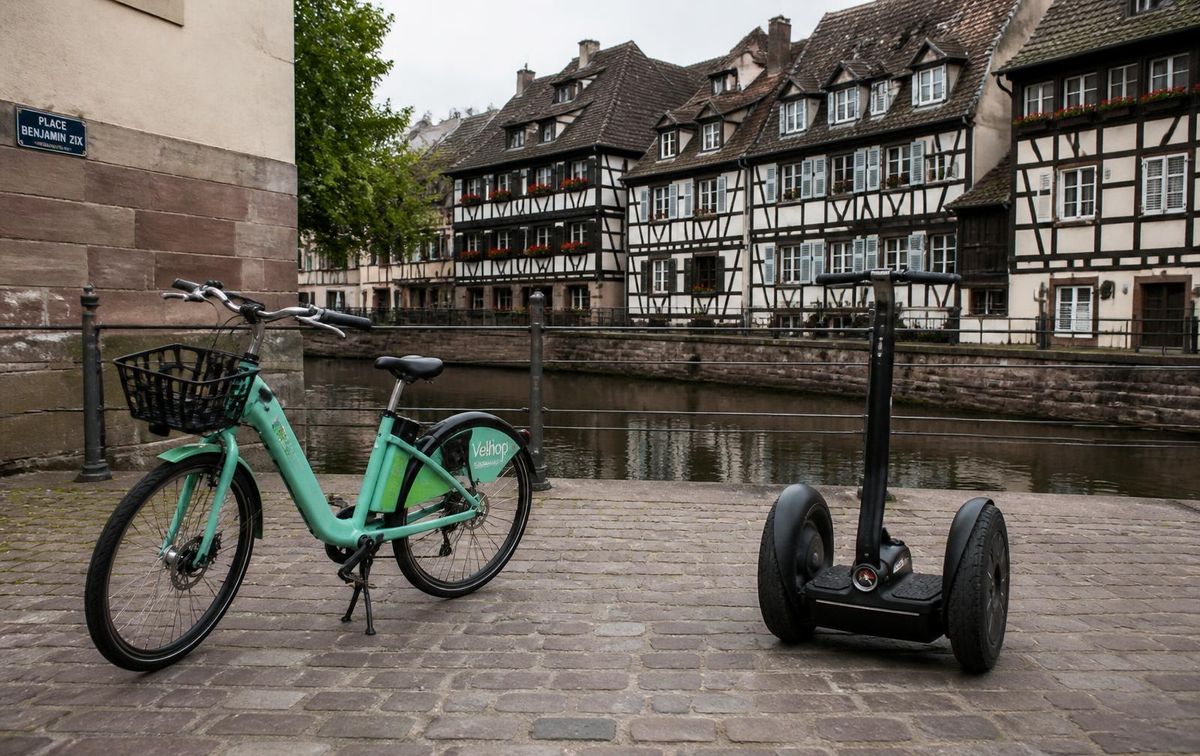 Ein elektrisches Stadtrad und ein selbstbalancierender Stehroller nebeneinander auf einem Platz an einem Straßburger Kanal