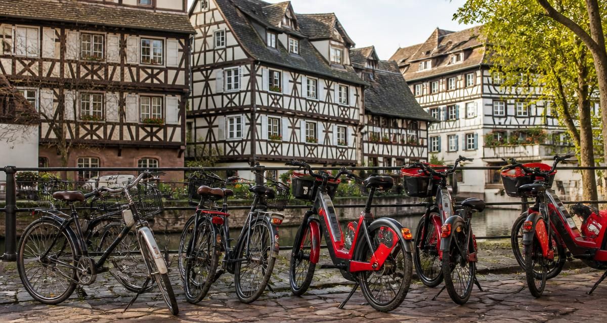Citybikes und rote E-Bikes stehen an einem Kopfsteinpflaster-Kai in der Petite France in Straßburg