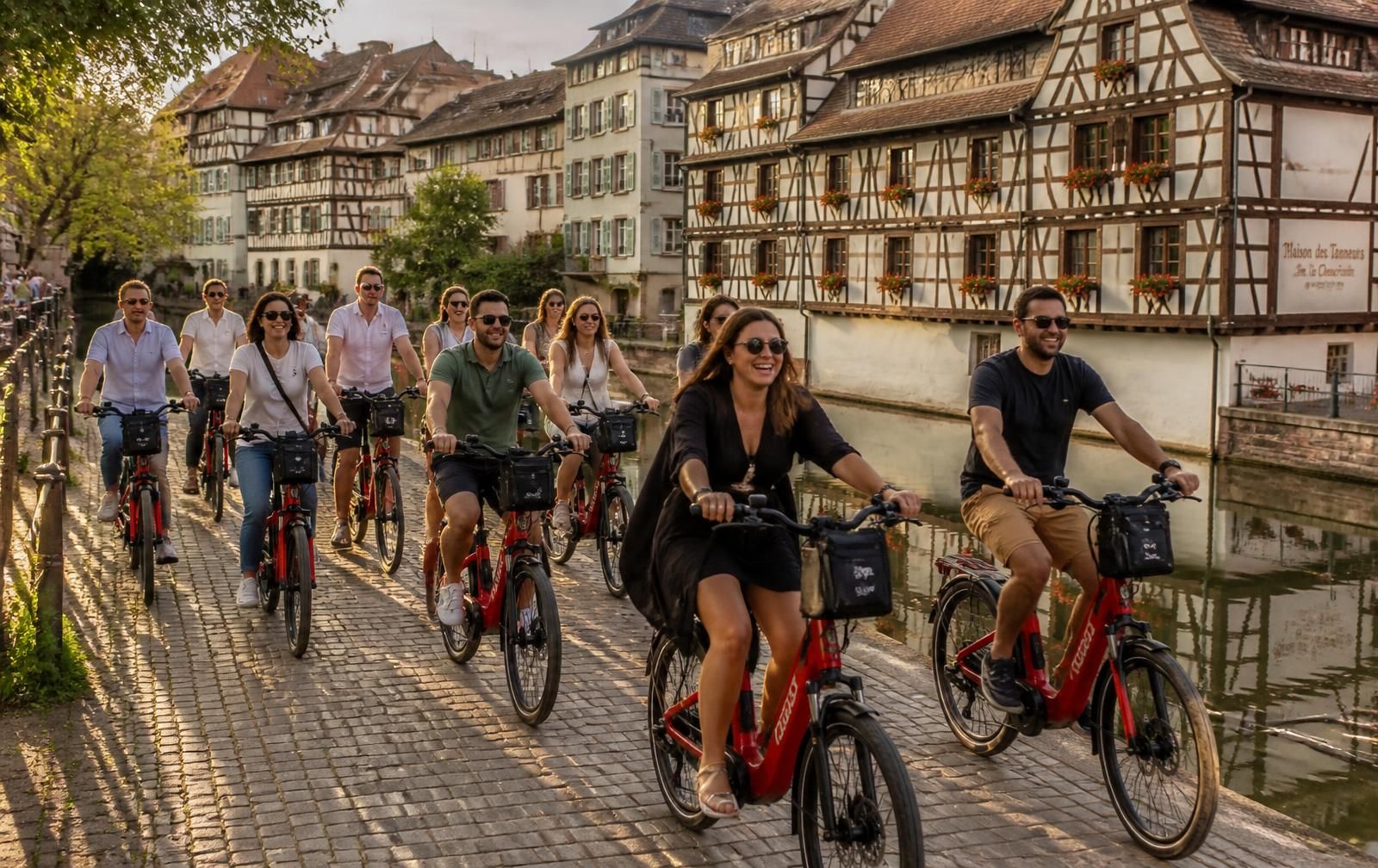 Eine Gruppe fährt auf roten VéloRouge-E-Bikes am Wasser in Straßburg entlang